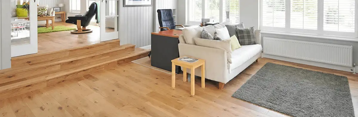 A modern living room with professionally installed laminate flooring, a beige sofa, a small side table, a gray rug, and large windows with white shutters in Scottsdale, AZ